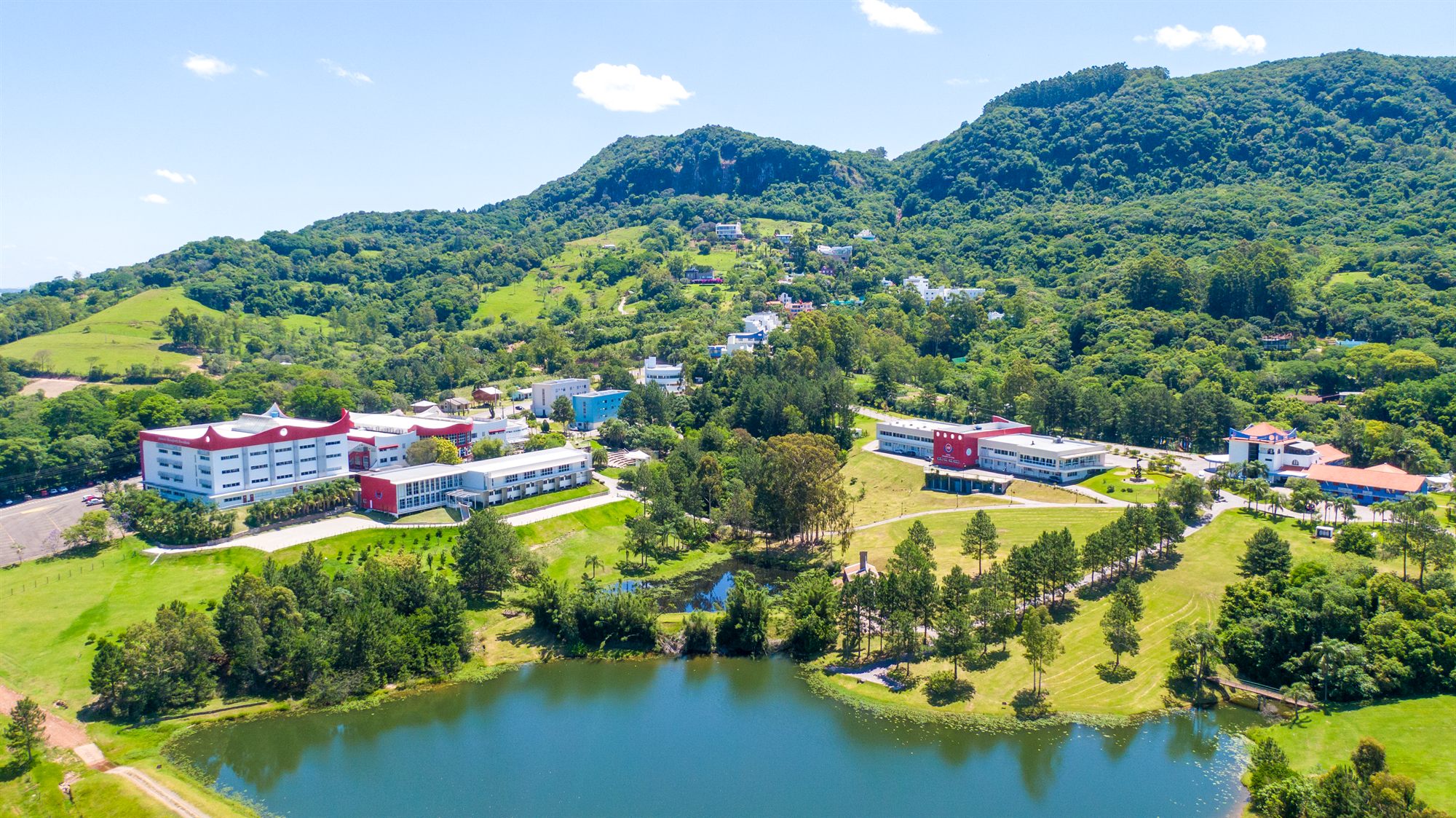 Vista aérea do campus da AMF no Recanto Maestro, com o lago em primeiro plano e a serra ao fundo